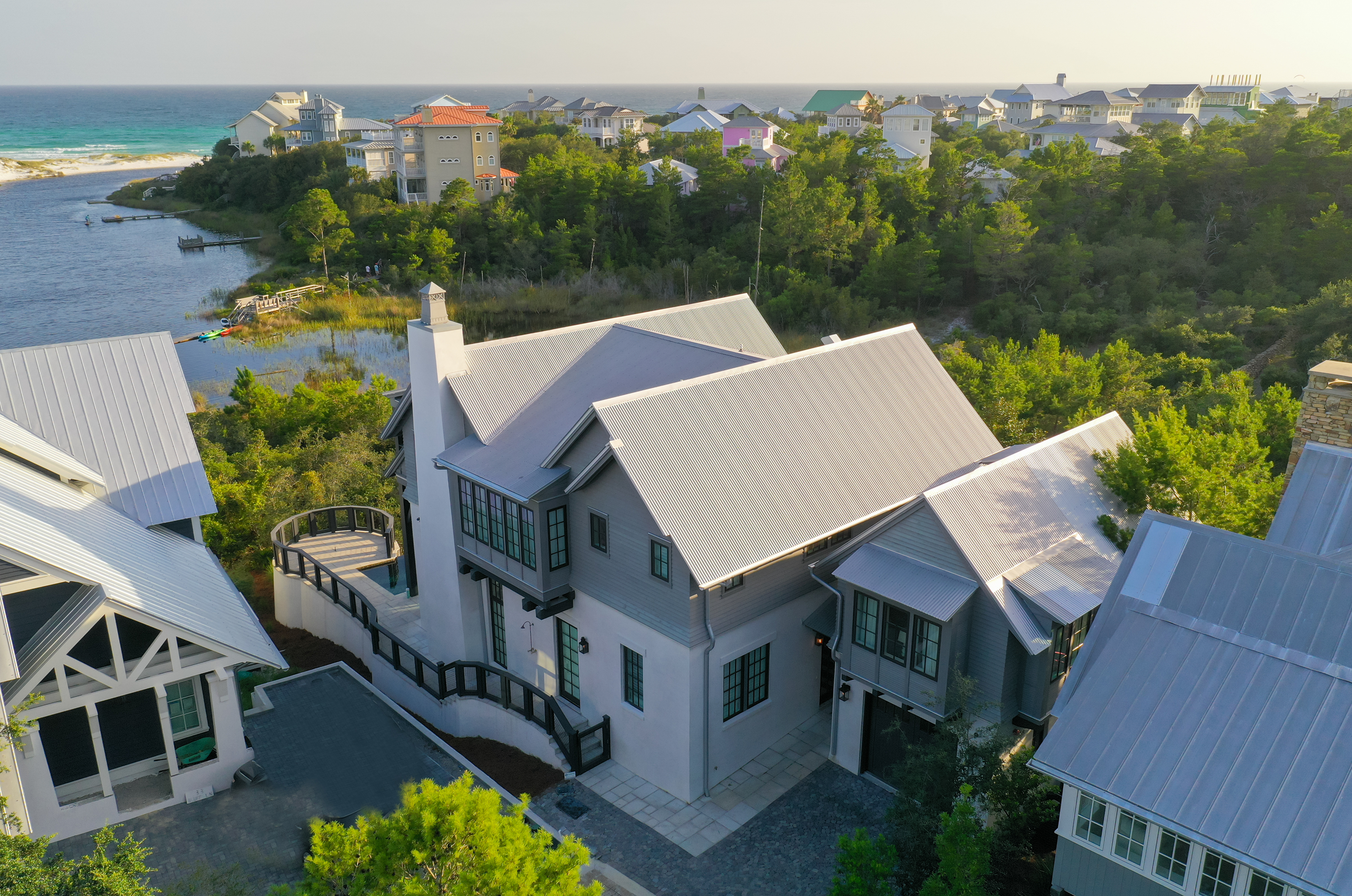 Aerial view of houses near a body of water with green trees and distant ocean.