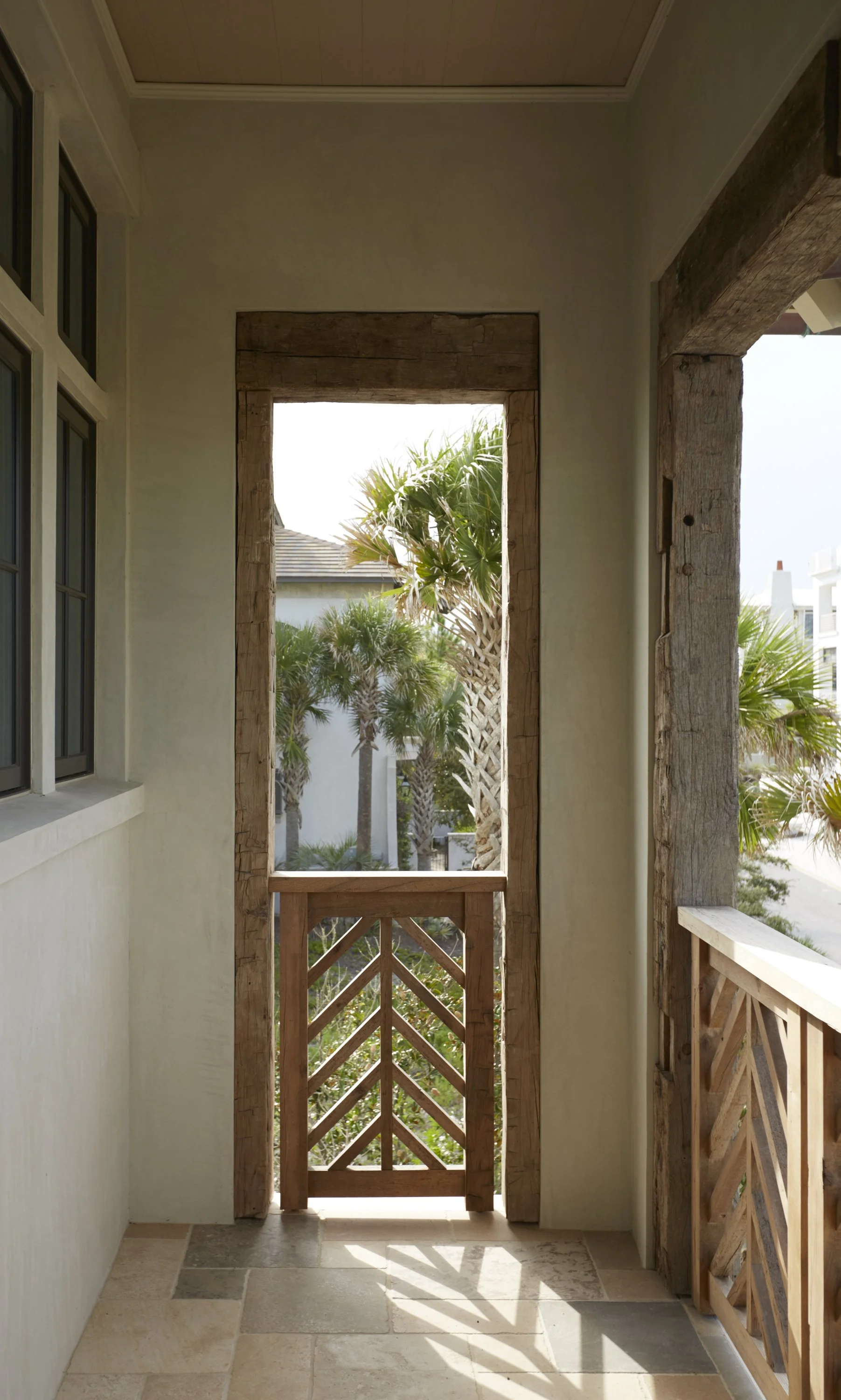 A view from a balcony with wooden railings of palm trees and tropical plants outside.