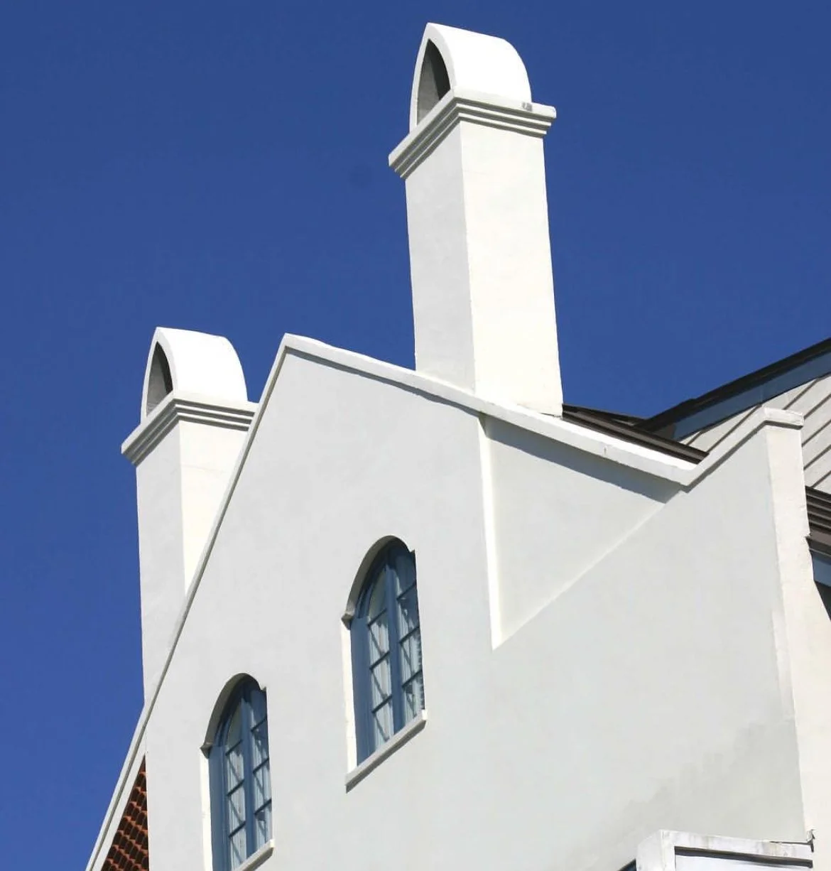 Close-up of a white house with arched windows and two prominent chimneys against a clear blue sky.