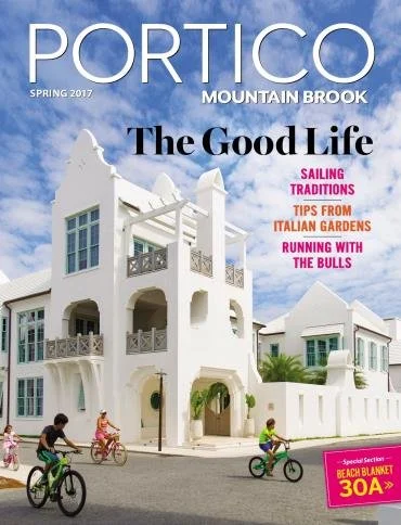 Cover of PORTICO magazine, Spring 2017 issue, Mountian Brook edition, featuring a white Mediterranean-style building and children riding bicycles on the street, with headlines about sailing traditions, Italian gardens, and running with bulls.