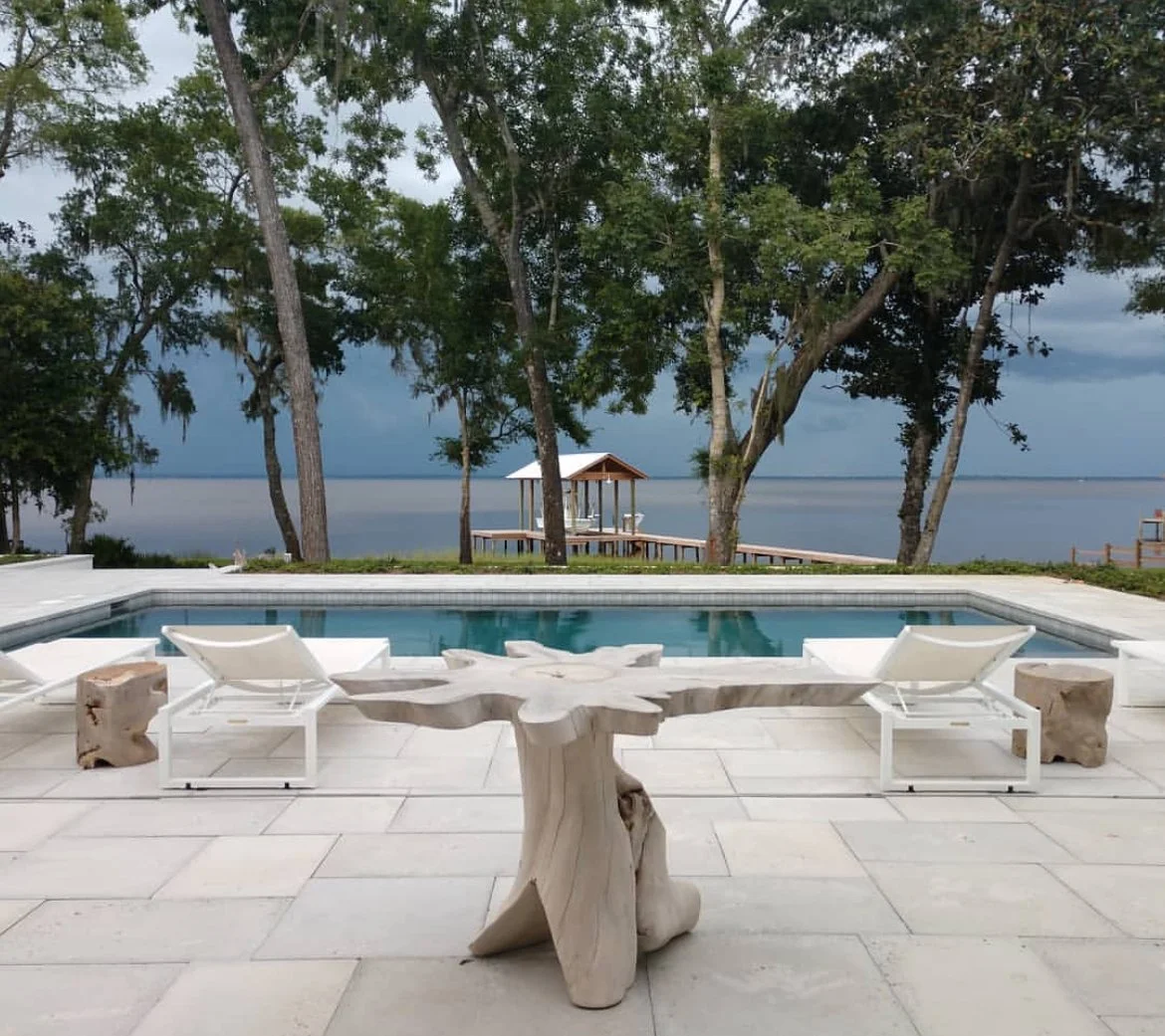 A backyard with a swimming pool overlooking a lake, with trees and a gazebo on the lake's shore.