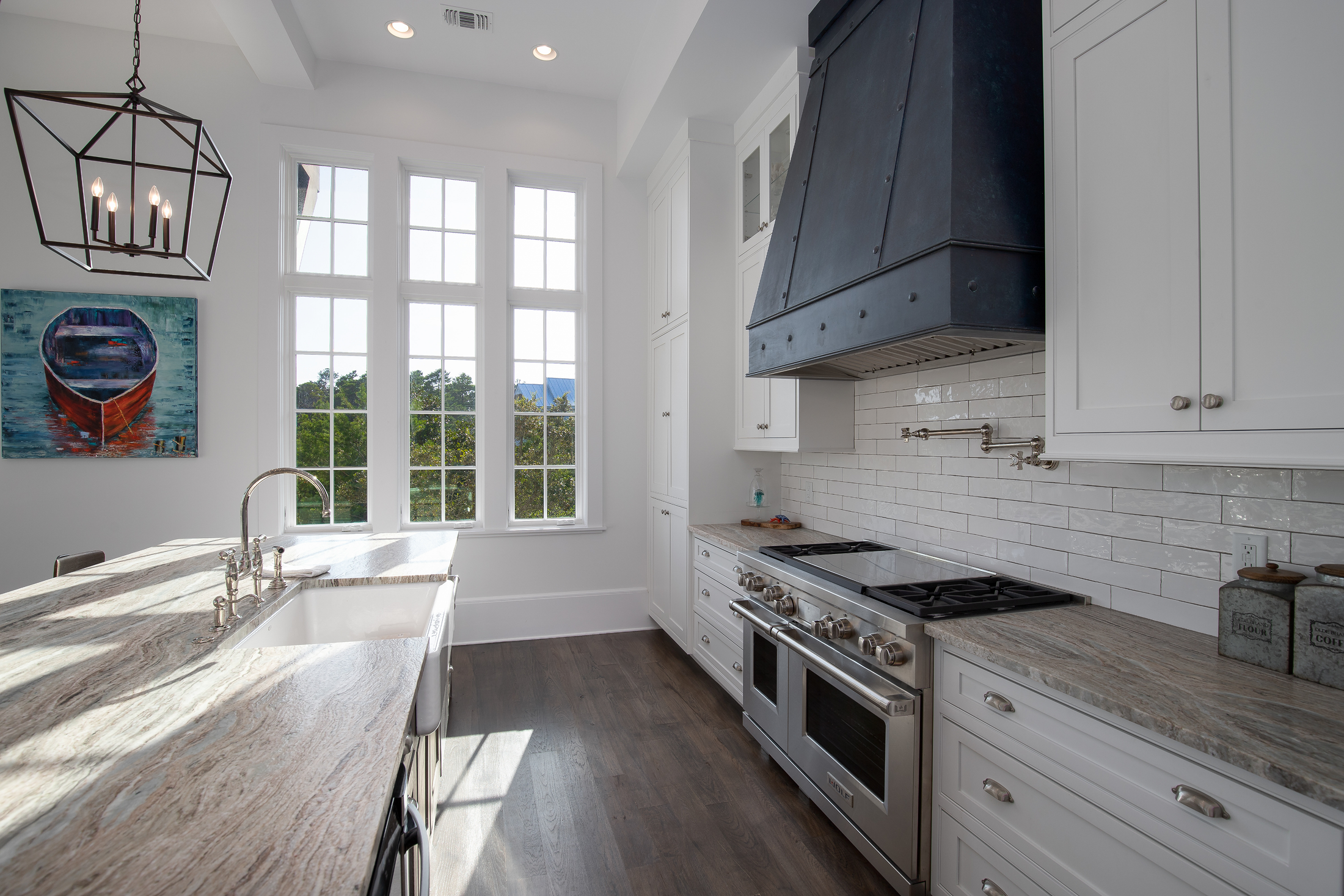 Bright kitchen with large windows, white cabinets, stainless steel oven, dark wood floors, and a modern black range hood.