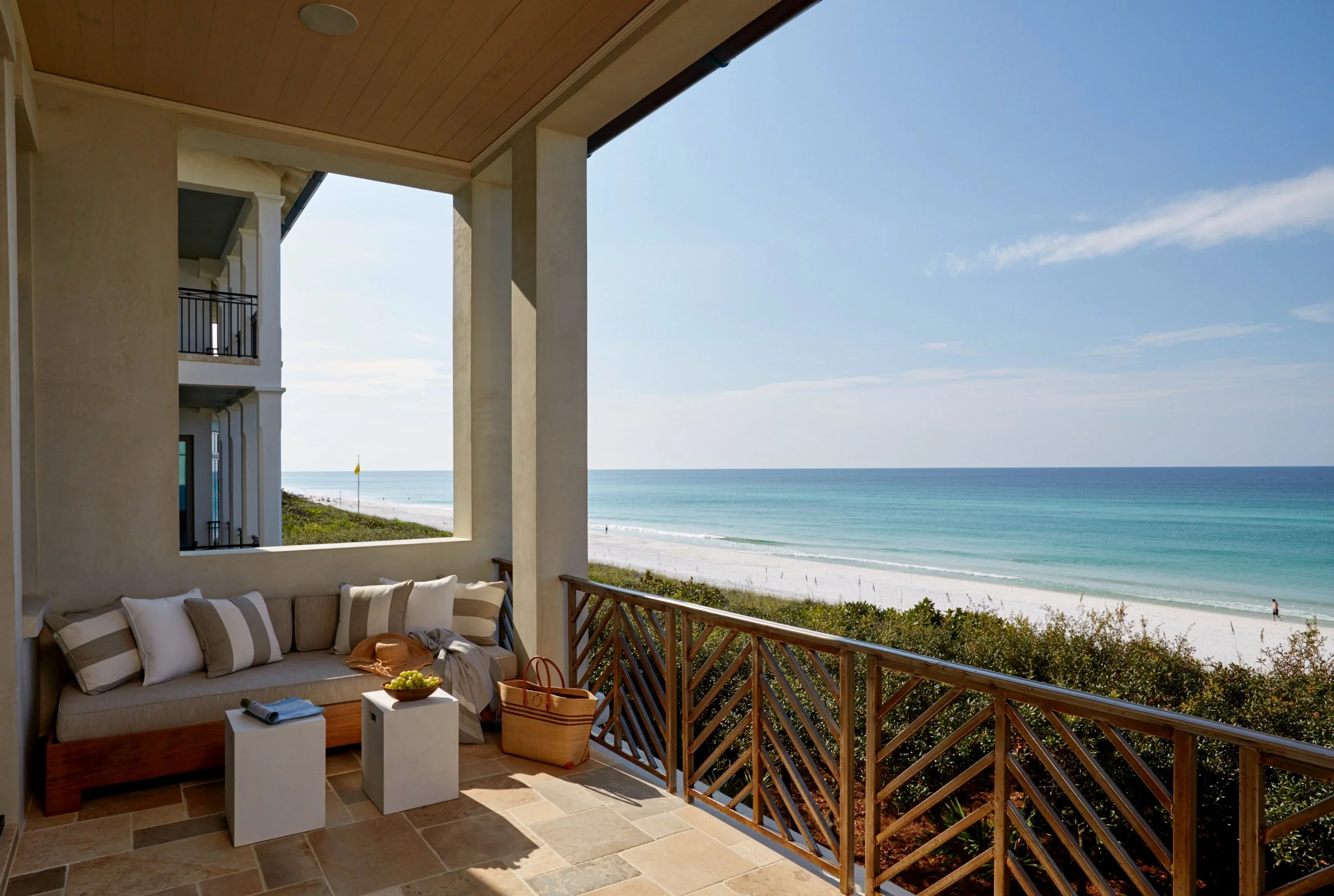 Balcony with a seating area overlooking a beach with white sand, green shrubs, and the ocean.