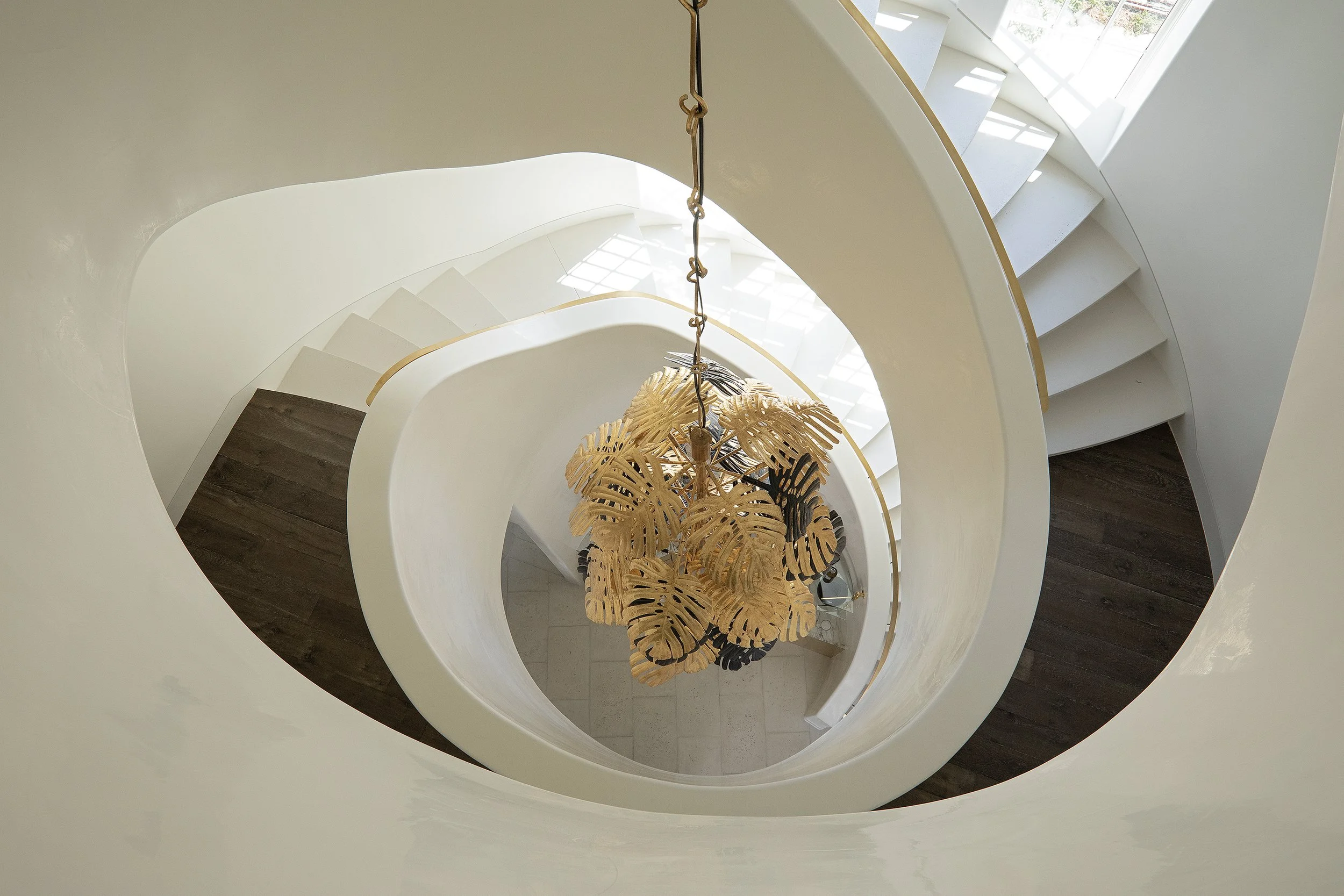 A spiral staircase viewed from above with a hanging leaf-shaped chandelier in the center.
