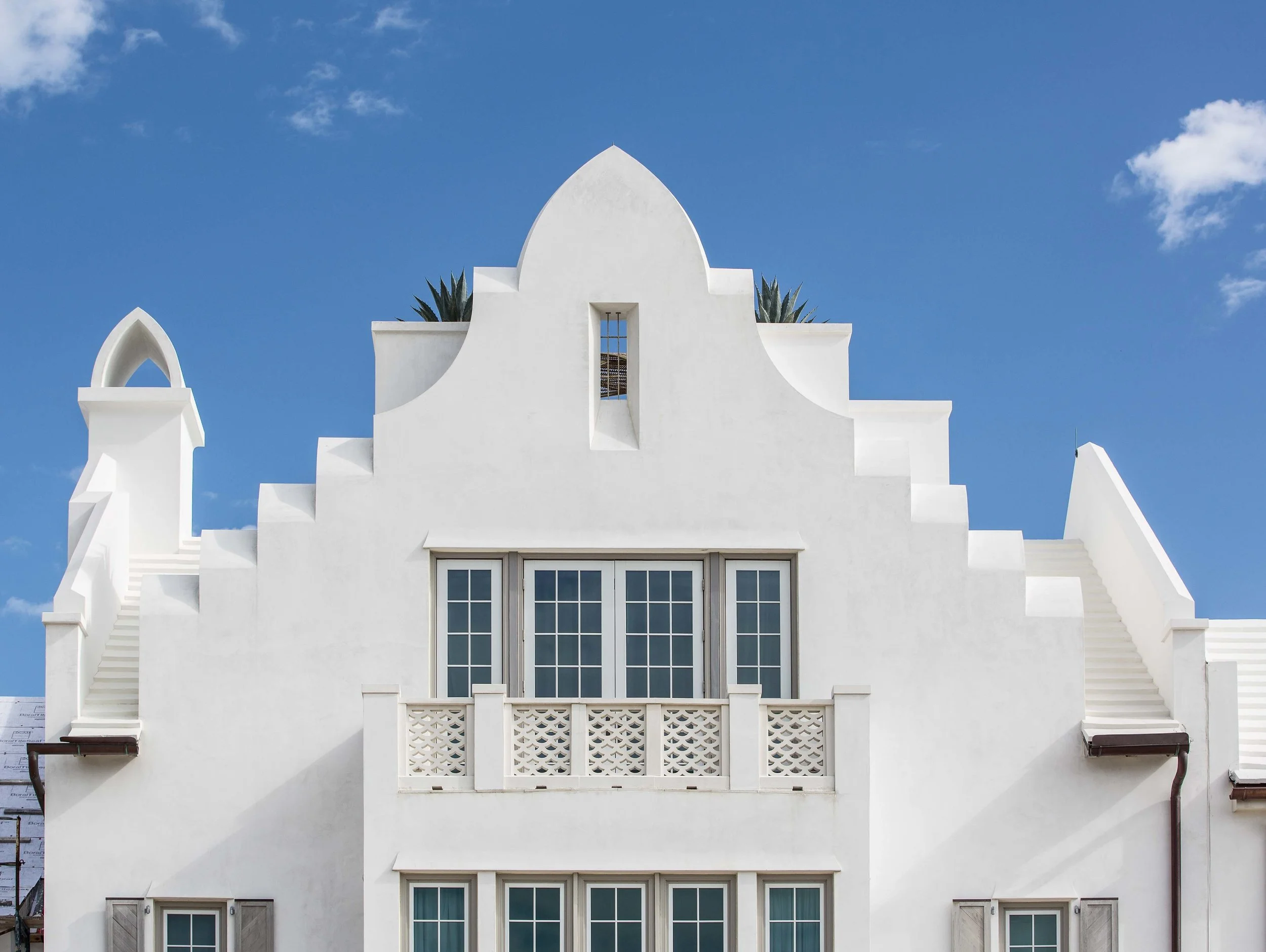 White Mediterranean-style building with arched architectural features and multiple balconies, under a blue sky with a few white clouds.