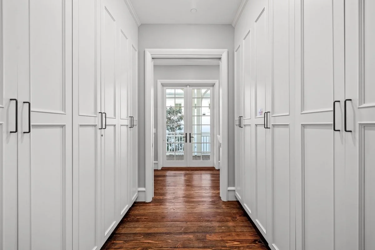 A bright hallway with white paneling on the walls, dark hardwood floors, and glass double doors leading outside.