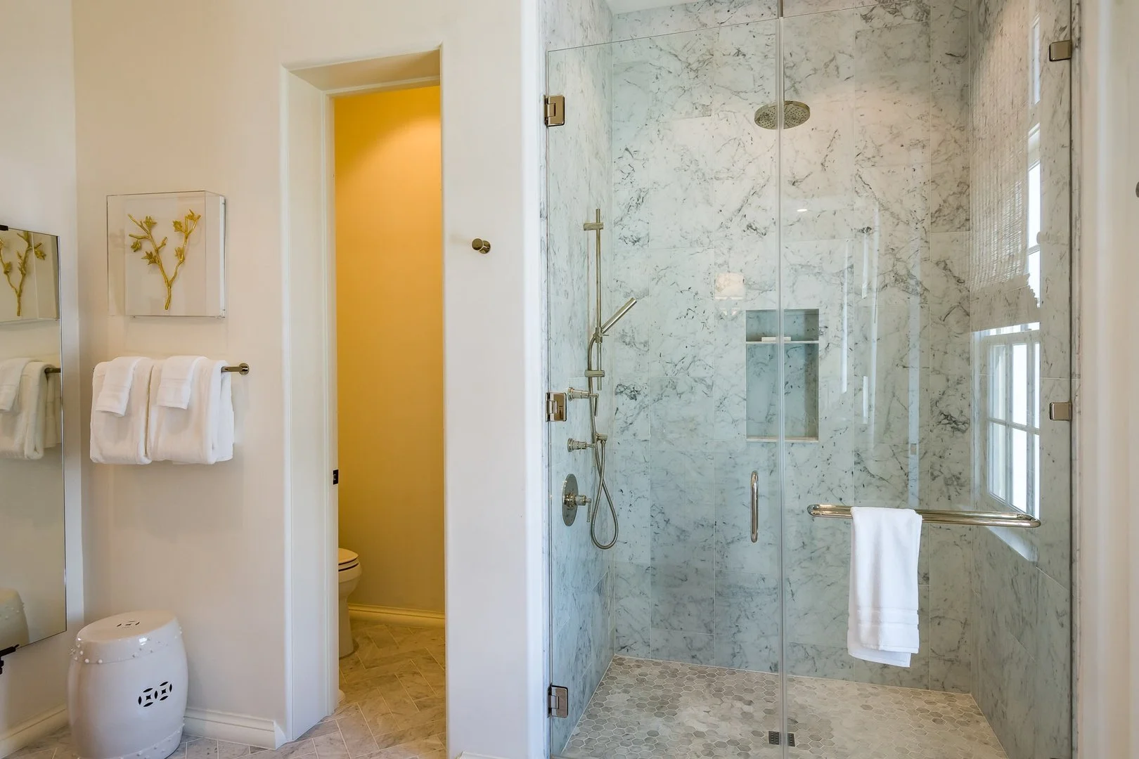 Bathroom with a glass-enclosed marble shower, white walls, a towel rack with white towels, and a small bench or stool