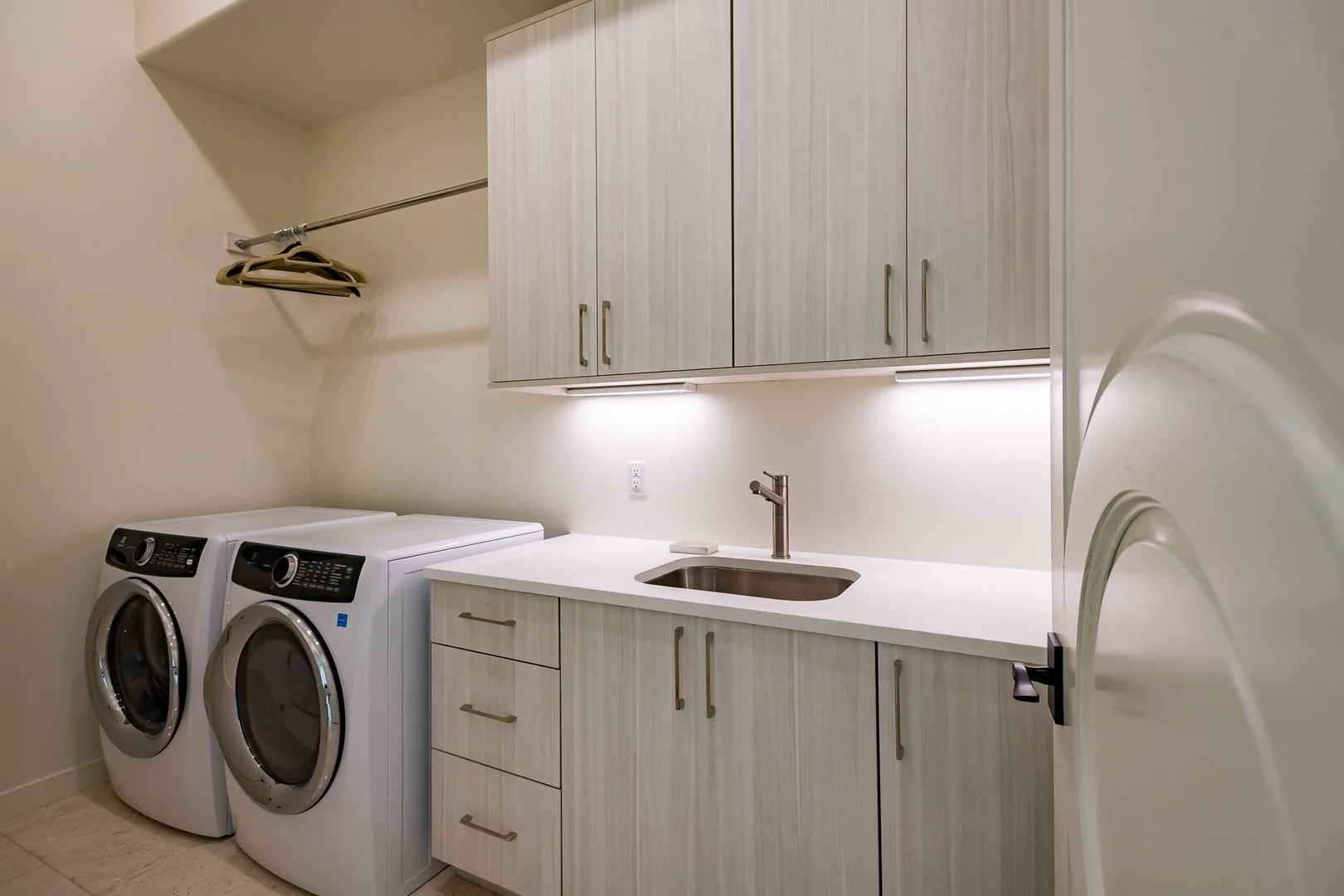 Laundry room with washer and dryer, white cabinets, a sink, and a small shelf with hangers.
